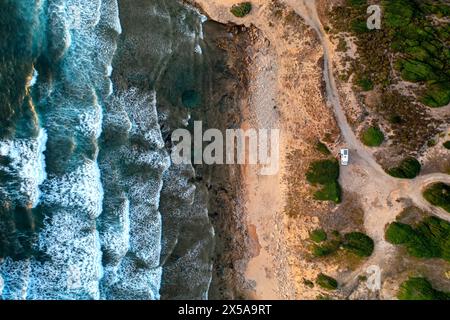 Stunning drone shot capturing the contrasts of a remote Sardinian beach with foaming waves and a solitary vehicle Stock Photo
