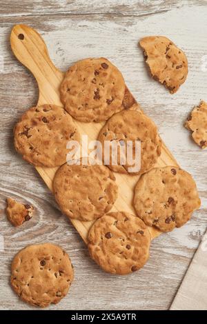 A tantalizing top view of fresh-baked chocolate chip cookies arranged neatly on a rustic wooden cutting board, with cookie crumbs scattered around Stock Photo