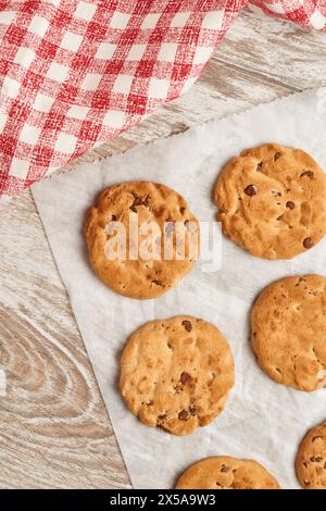 Chocolate chip cookies laid out on parchment paper with a classic gingham cloth beside them, captured from a top-down perspective Stock Photo