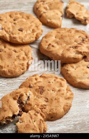 Artisanal chocolate chip cookies with a golden hue, displayed invitingly on a textured wooden surface, some with a bite taken out Stock Photo