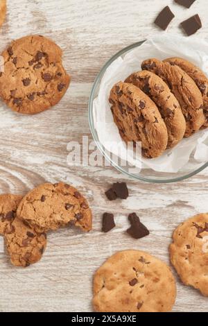 Chocolate chip cookies in a glass bowl and scattered on a rustic wooden table, photographed from above Stock Photo