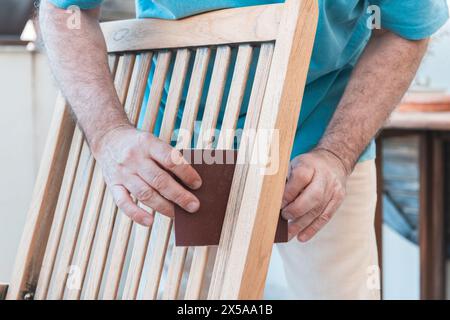 Close-up of a man skilfully sanding a wooden chair, preparing it for varnishing in a workshop Stock Photo