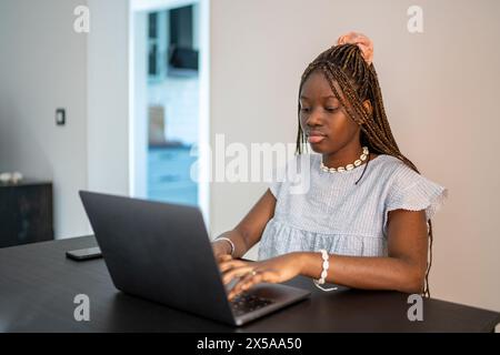 An African American woman focused on her work while using a laptop at home, illustrating the telecommuting lifestyle Stock Photo