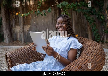 A joyful African American woman works from home, sitting outside with a digital tablet Stock Photo