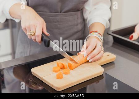 Anonymous person prepares a roast chicken with vegetables in a cozy Madrid kitchen, focused on slicing carrots Stock Photo