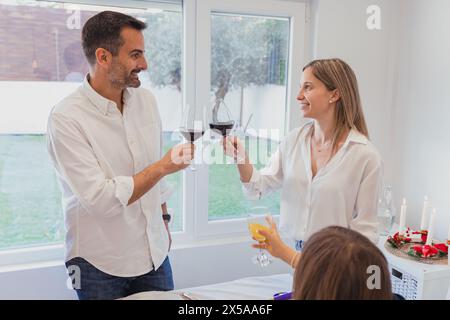 A man and woman cheerfully toast with red wine glasses at a festive family Christmas meal set within a cozy home environment Stock Photo