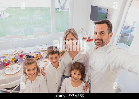 A cheerful family captures a moment with a selfie during their festive Christmas meal at a beautifully set home table Stock Photo