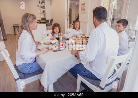 A happy family enjoys a Christmas meal together at home, with a festive table setting and holiday decorations Stock Photo