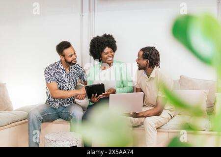 Three diverse professionals engaging in a collaborative work session in a bright coworking environment, sharing ideas with digital devices Stock Photo