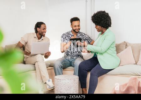 Three professionals engaging in a collaborative work session on a couch with digital devices Stock Photo