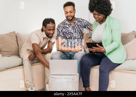 Two men and a woman work together on a couch, one using a laptop and the other a digital tablet, representing a co-working environment Stock Photo