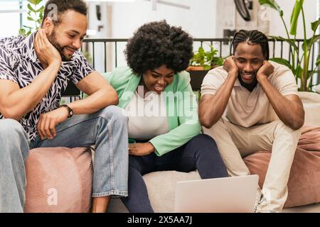 Three young professionals engaging in collaborative work on a laptop in a modern coworking space Stock Photo