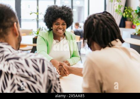 Two professionals engaging in a warm handshake in a bright coworking space, reflecting positive collaboration and networking Stock Photo