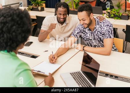 Three colleagues engage in a discussion at a well-lit coworking environment complete with modern furnishings and laptops Stock Photo