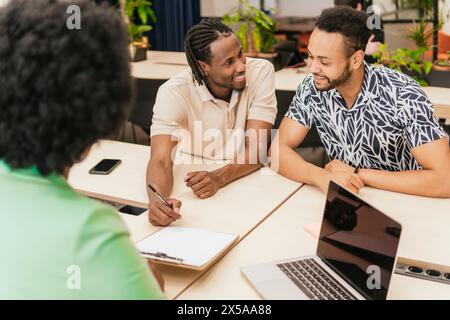 Three professionals collaborate warmly at a coworking space, sharing ideas and using digital devices Stock Photo