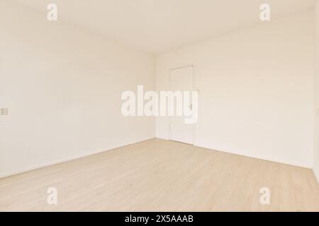 An empty, bright room with a white door, featuring a wooden laminate floor and clean white walls under soft light. Stock Photo