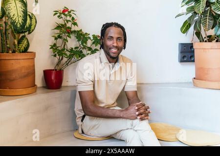 Man smiling in a modern, plant-filled coworking space, radiating a relaxed atmosphere Stock Photo