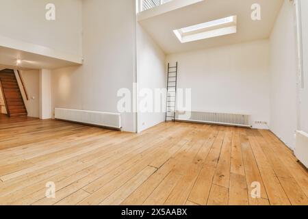 An empty room featuring natural wood flooring, white walls, a skylight, and a staircase with a loft area. Stock Photo