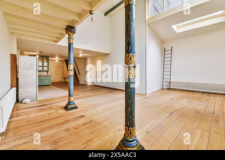 An expansive, well-lit room featuring hardwood floors, a painted ornamental column, and a loft-style staircase. Stock Photo