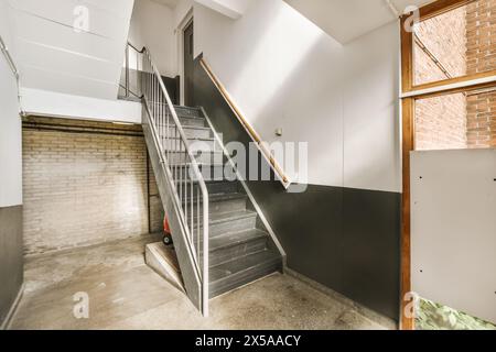 An industrial-style staircase with metal railings, exposed brick wall, and large window providing natural light. Stock Photo