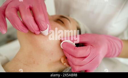 Before the ultrasonic facial cleansing procedure, a professional cosmetologist applies a film to the client s face. Before the procedure, the Stock Photo