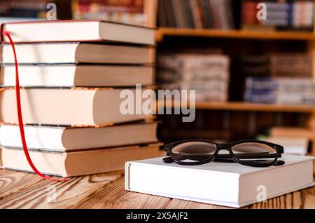 ok stacked with Eyeglasses on wooden Table with blurred Bookshelf in library room Area at Home Stock Photo