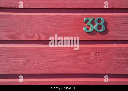 Close up shot of brass number 38 on red painted weatherboards of a beach hut Stock Photo