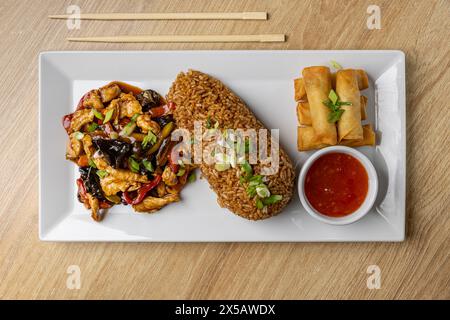 Savory platter featuring fried rice, spring rolls, and stir-fried vegetables served on a wooden table Stock Photo