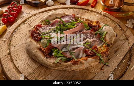 Artisan pizza with sun dried tomatoes, prosciutto, arugula, and cheese, served on rustic wood Stock Photo