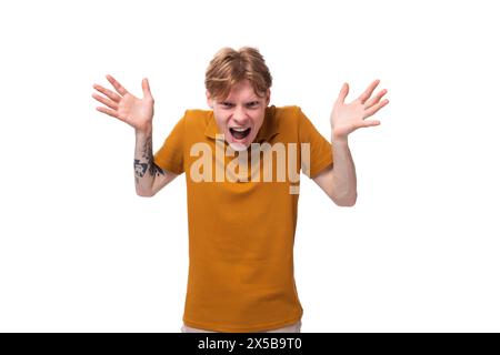 a young frustrated guy with short red hair dressed in a summer orange T-shirt is shouting with his hands up Stock Photo