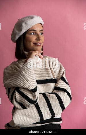 A woman in striped sweater and white beret smiles in front of pink background Stock Photo