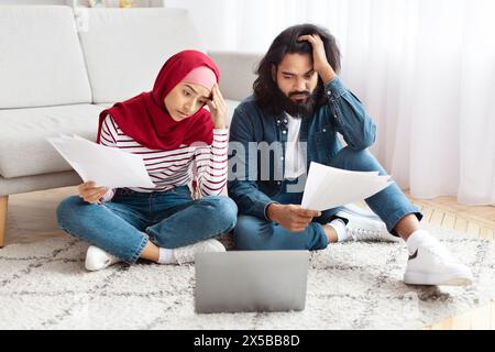 Worried Couple Reviewing Documents Next to a Laptop Stock Photo
