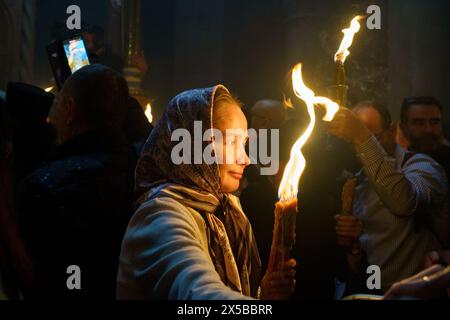 A young devotee holding candles with the Holy Fire during the Holy Fire Ceremony. The Holy Fire ceremony is celebrated by orthodox churches in the Church of the Holy Sepulchre in Jerusalem every year before Easter. This spiritual and religious event is one of the most important rituals of the orthodox Christianity, and many pilgrims gather from all around the world to witness it. During the ceremony the Greek Patriarch enters the aediculae where Jesus tomb is located, praying until the holy fire is believed to be lit by the Holy Spirit. The crowds at the church wait outside eagerly to witness Stock Photo