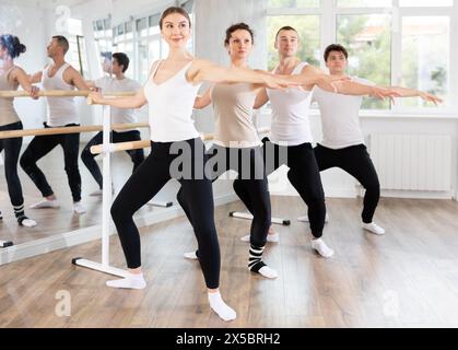 Woman practicing demi plie at barre at group ballet class Stock Photo