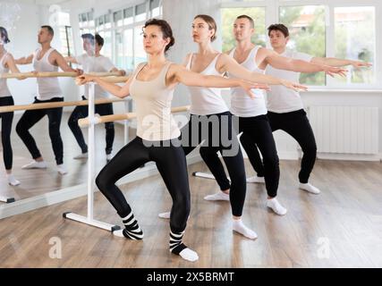 Woman practicing demi plie at barre at group ballet class Stock Photo