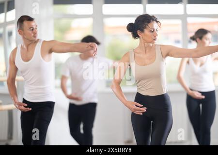 Graceful happy woman in sportswear confidently leading ballet class with dancers following her movements in dance studio Stock Photo