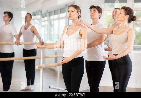 Group of ballet enthusiasts practicing at barre with experienced ballerina Stock Photo
