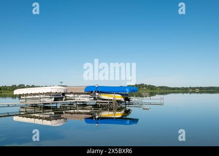 Docked boats on lifts are reflected in the calm water of a pretty lake in Minnesota, on a sunny summer day with beautiful clear blue sky. Stock Photo