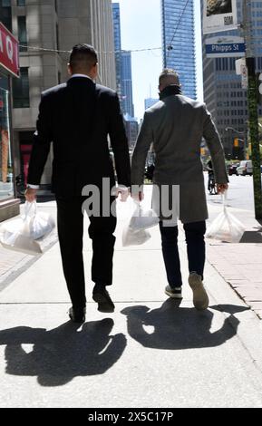 Two men in business suits walk down a city street carrying plastic bags with lunch dishes inside Stock Photo