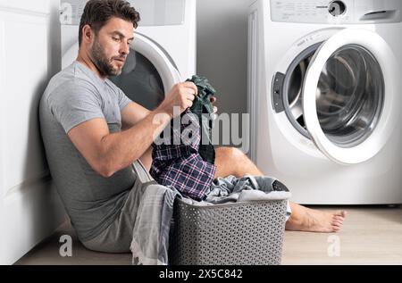 Man with clothes near washing machine. Laundry cleaning. Housework, homework, male housekeeper. Husband man doing laundry at home. Washer and dryer at Stock Photo