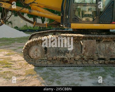 Low view of yellow Tracked Excavator in grass and dirt with a pile of small white stones on the left. Paint scrapes and dirt on tracks. Horizontal Stock Photo