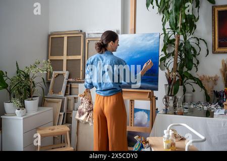 Focused woman artist working on oil picture. Rear view, female painter drawing at art workshop. Stock Photo