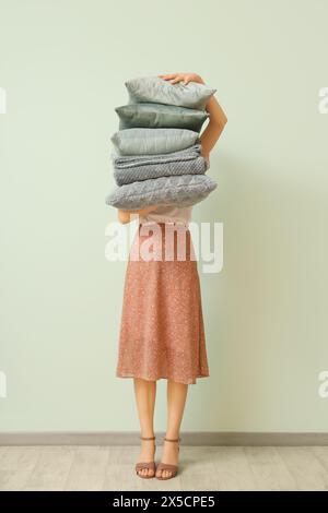 Woman with stack of pillows and folded warm plaid near light wall Stock Photo