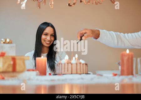 Woman, happy and lighting candles on cake for birthday, celebration and pride in apartment for life event. Female person, smile and party with couple Stock Photo