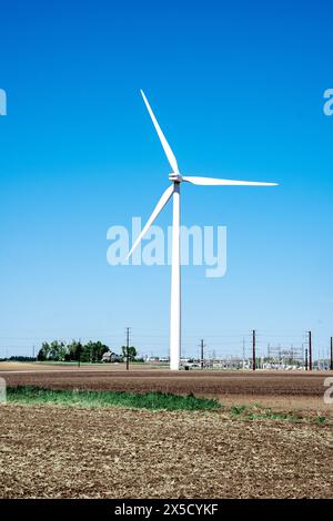 A single wind turbine stands tall in a vast agricultural field under a clear blue sky, symbolizing renewable energy in rural settings. Stock Photo