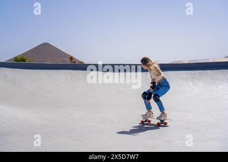 Woman with a skateboard is skillfully riding down the side of a ramp in a skateboard park. Stock Photo
