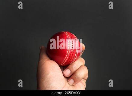 red cricket leather ball in bowler's hand on the dark background Stock Photo