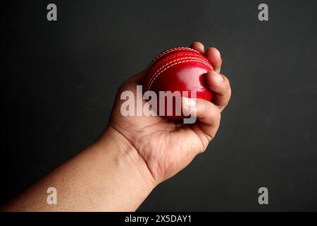 red cricket leather ball in bowler's hand on the dark background Stock Photo