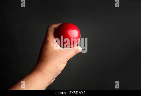 red cricket leather ball in bowler's hand on the dark background Stock Photo