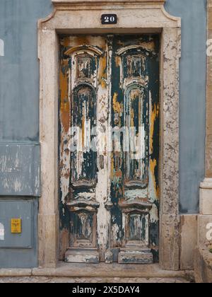 Peeling and flaking blue orange and white paint on old double wooden doors at 20 Rua Vasco da Gama Olhão, Algarve, Portugal Stock Photo
